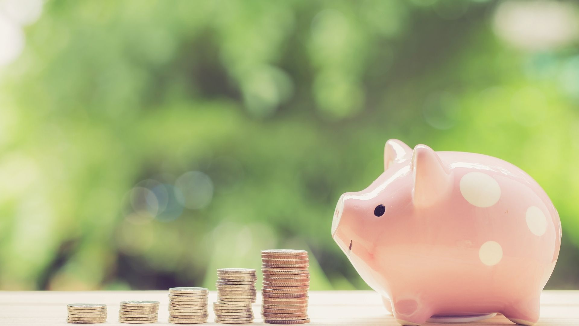 Pink piggy bank with stacked coins on wooden table