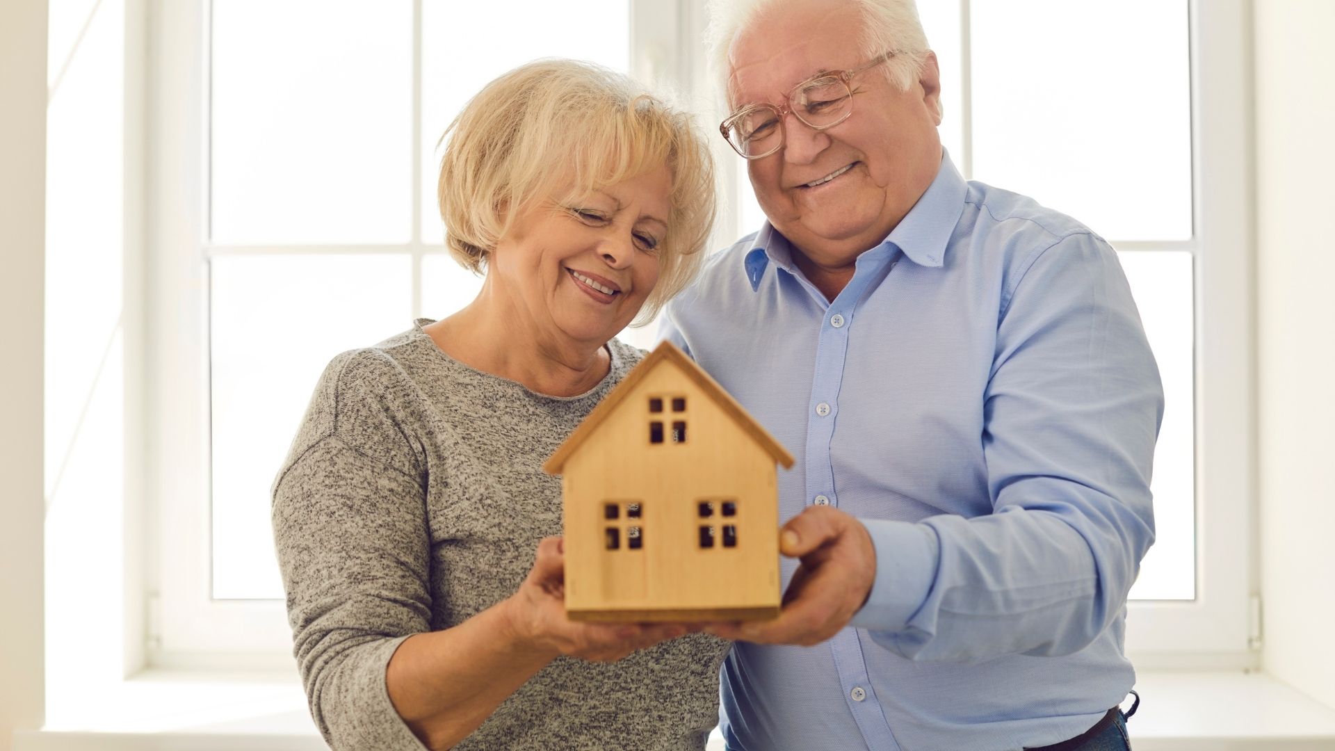 Elderly couple holding wooden house model