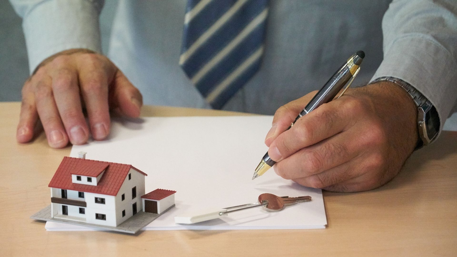 Man signing papers with model house and keys on table