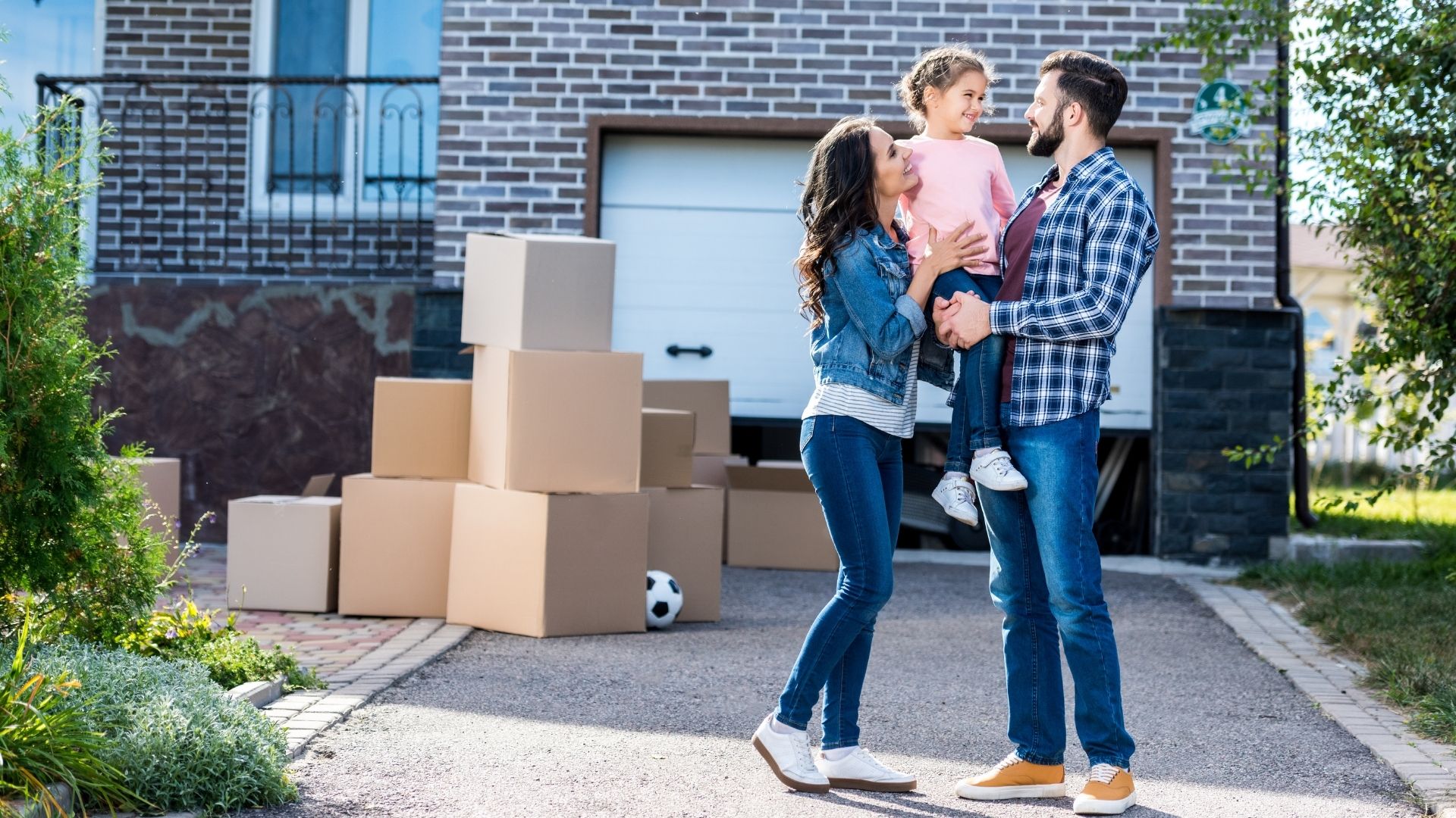 Family with child amidst moving boxes outside new home