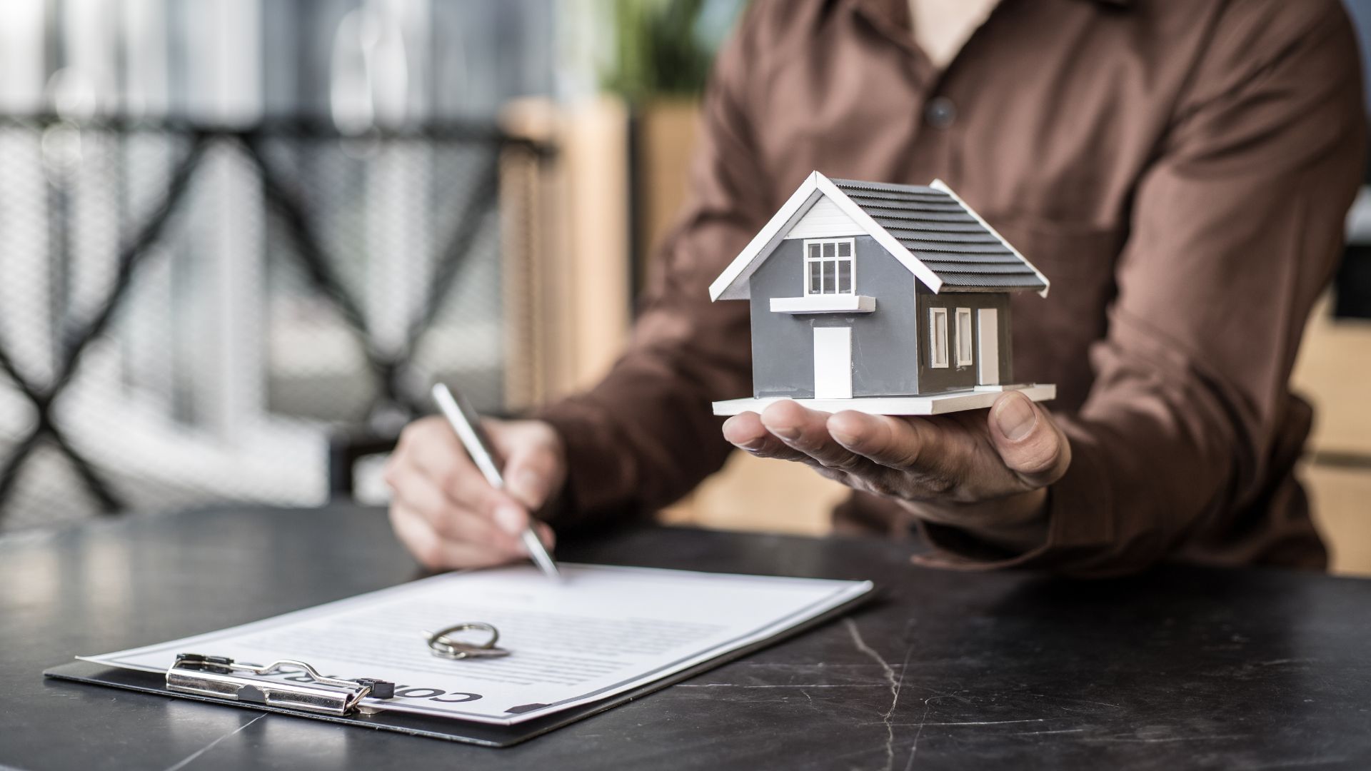 Man holding model house at desk with clipboard