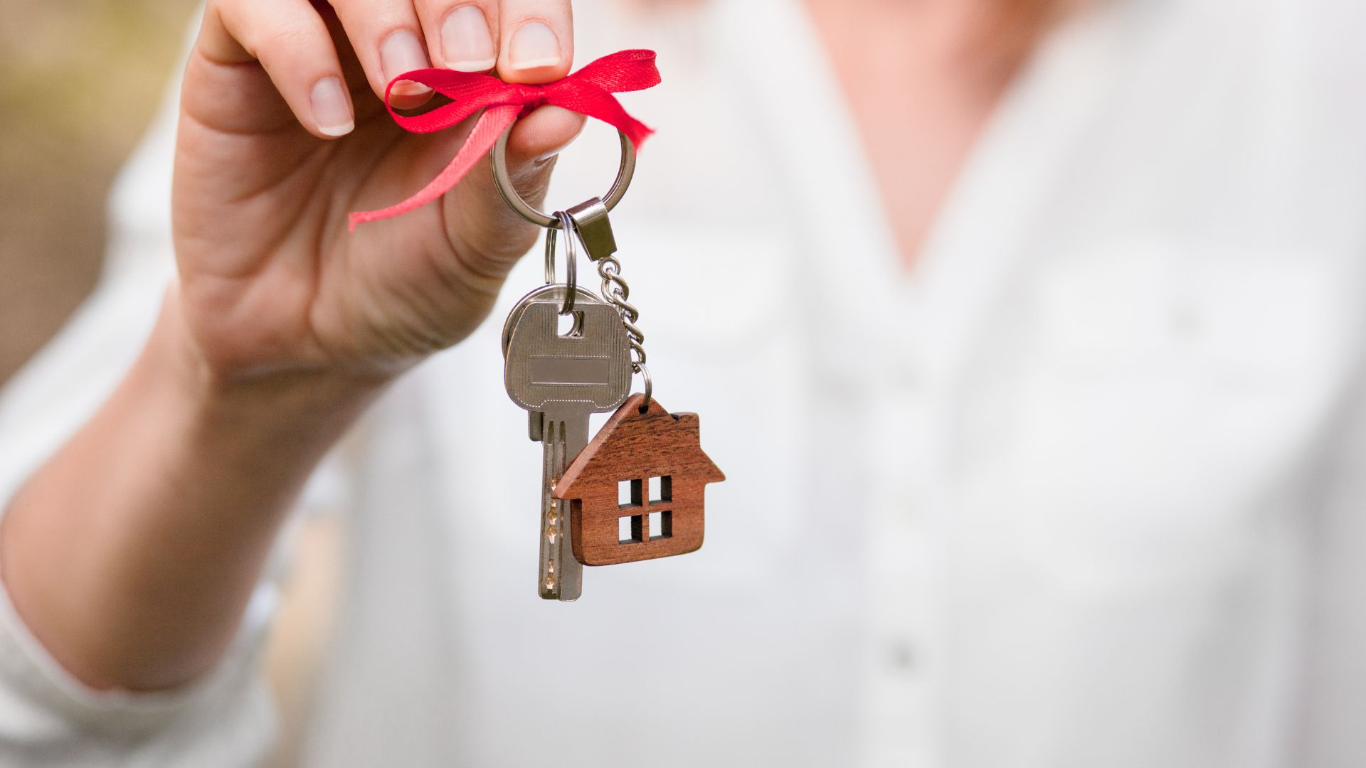 Hand holding keys with red ribbon and house charm