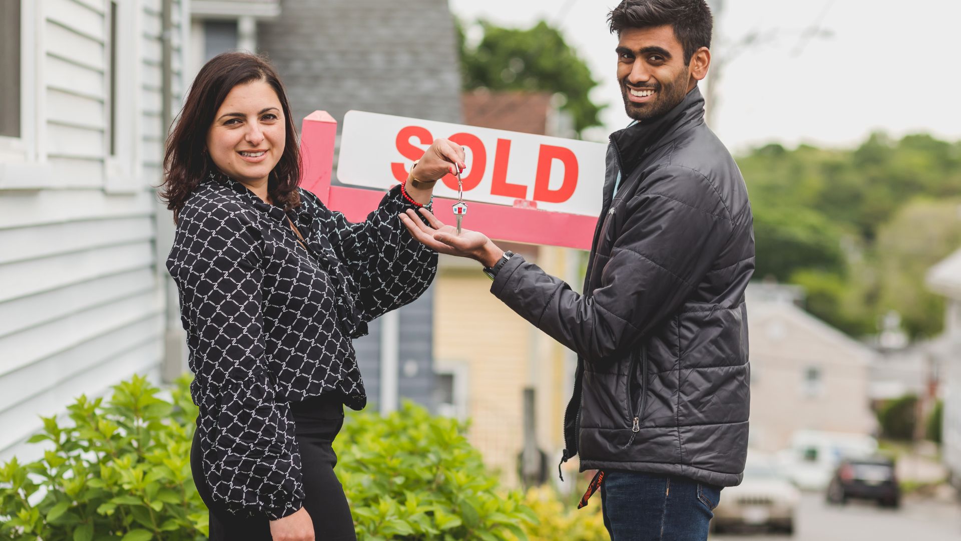 Couple holding house keys near sold sign